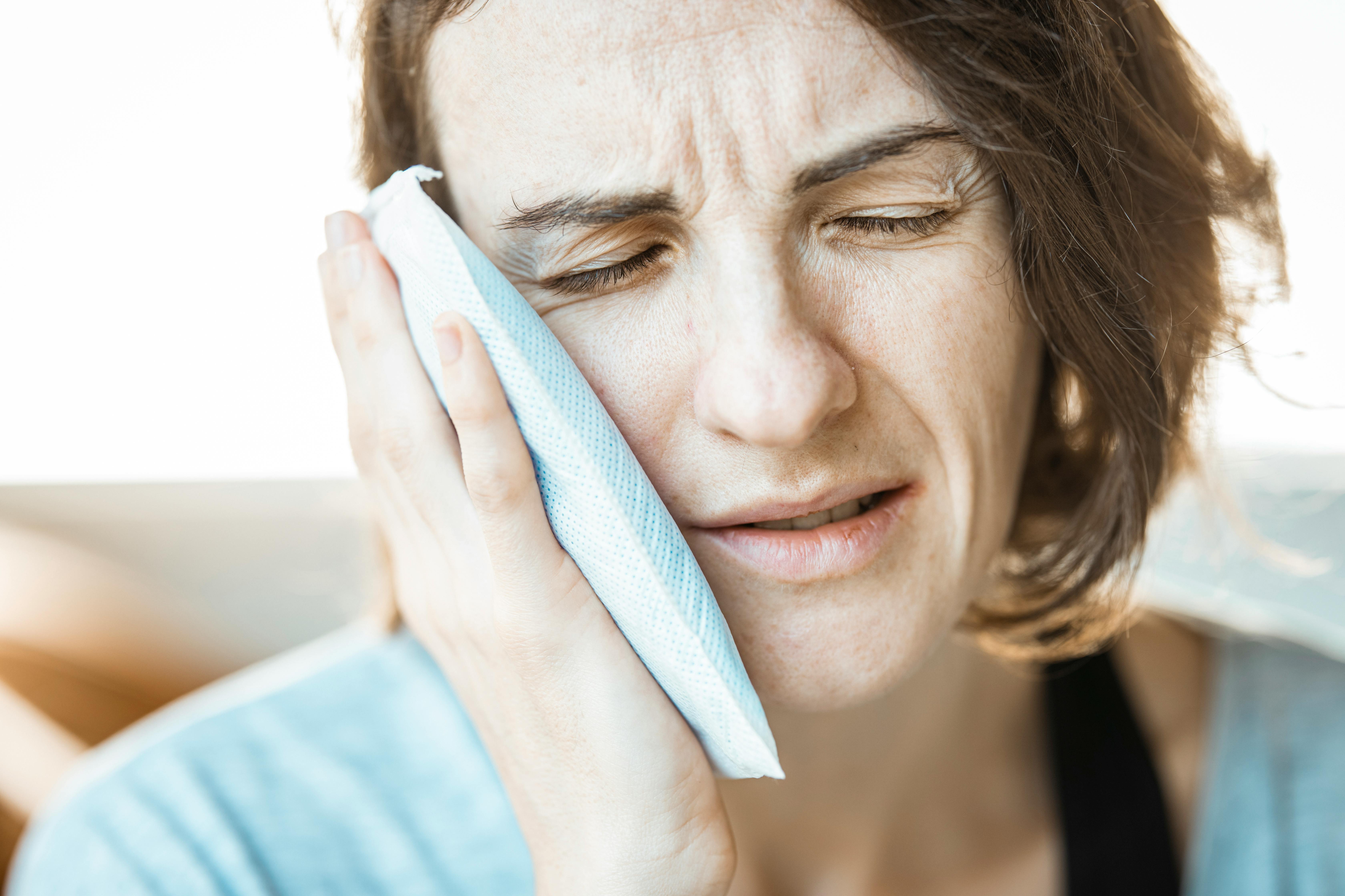 Woman Pressing Cold Pack Against Cheek With Pained Expression Indoors