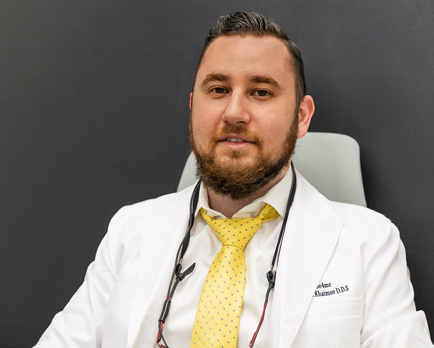 Photo Man In White Coat With Yellow Tie And Stethoscope Sitting In Chair Against Dark Wall