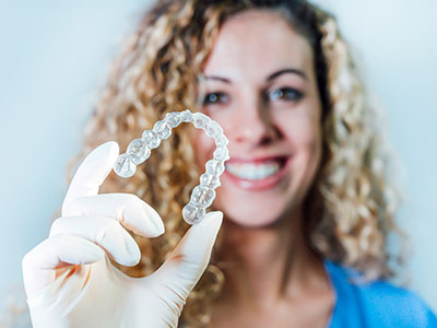 Photo Smiling Woman Wearing Glove Holding Clear Aligner Close Up Showing Benefits Of Invisalign In Dental Treatment