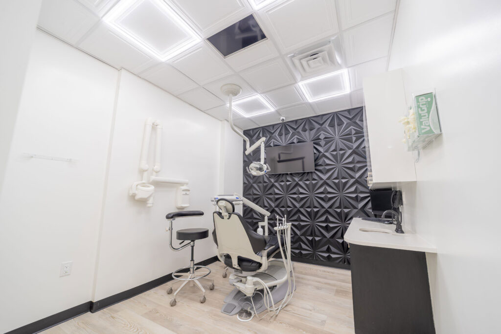 Photo Of Dental Treatment Room With Chair Overhead Light Stool Sink And Textured Black Wall Paneling