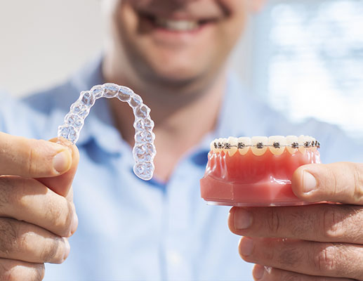 Photo Dentist Holding Clear Aligner And Braces Model Demonstrating Alternatives To Invisalign In Clinic Setting