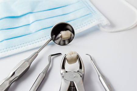 Photo Stainless Steel Forceps Holding Extracted Tooth Model Beside Dental Mirror And Surgical Mask
