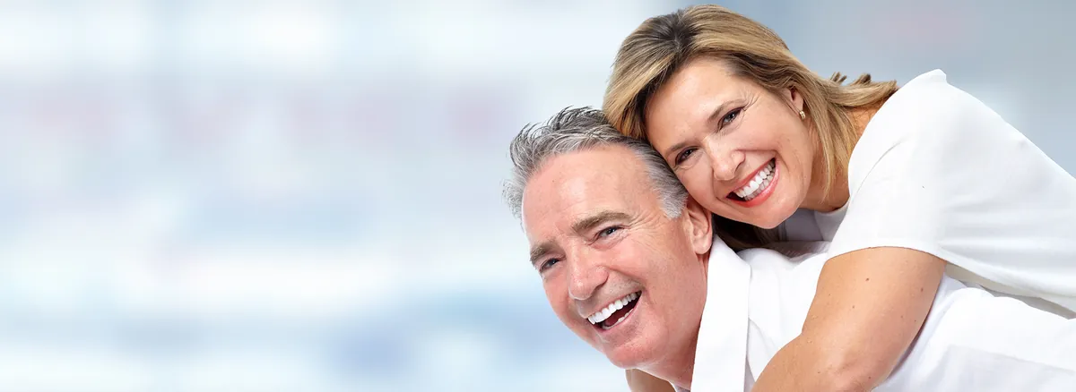 Smiling Middle Aged Couple Wearing White Clothing Posing Together Against Soft Blurred Background