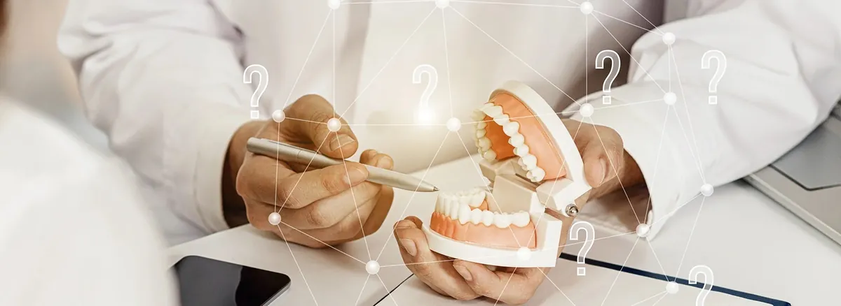 Dentist Holding Dental Model And Pen Explaining Treatment Options To Patient While Discussing How Much Does A Dental Implant Cost With Question Mark Graphics Overlaid